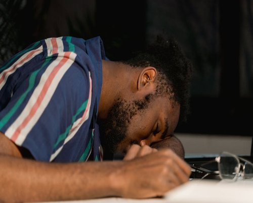 A person taking a nap or resting their eyes while leaning on a desk